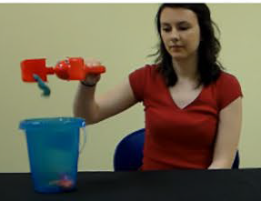 woman using a toy tool to drop other toys into a kids beach-type bucket